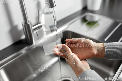 Image of woman washing hands with liquid soap in kitchen