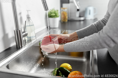 Image of woman washing fruits and vegetables in kitchen