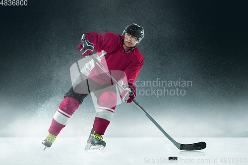 Image of Male hockey player with the stick on ice court and dark background