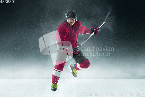 Image of Male hockey player with the stick on ice court and dark background