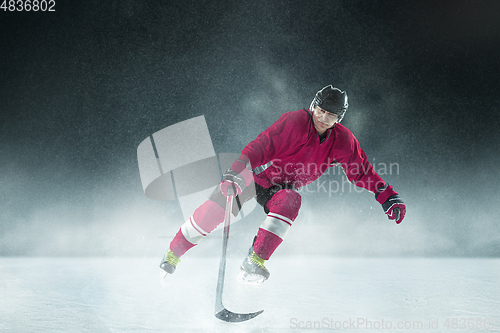 Image of Male hockey player with the stick on ice court and dark background