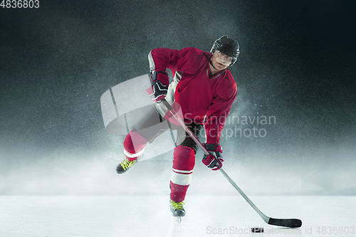 Image of Male hockey player with the stick on ice court and dark background