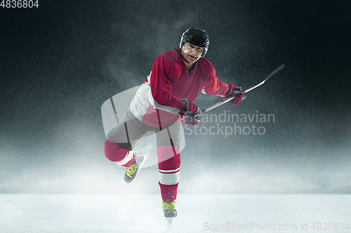 Image of Male hockey player with the stick on ice court and dark background