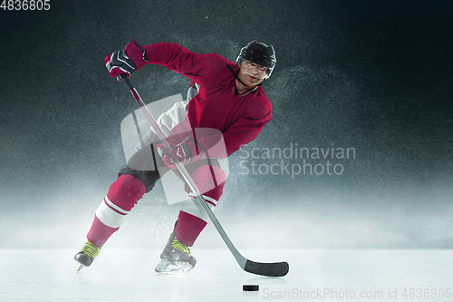 Image of Male hockey player with the stick on ice court and dark background