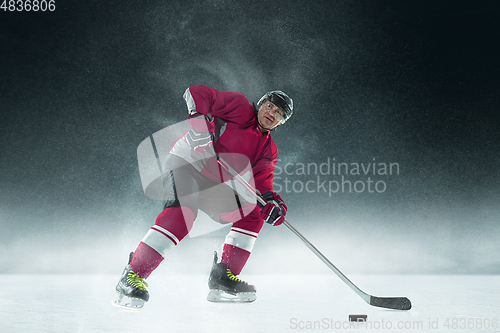 Image of Male hockey player with the stick on ice court and dark background