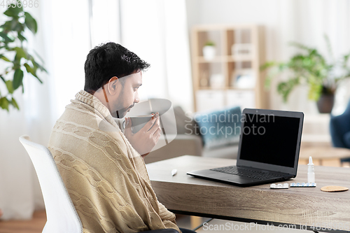 Image of sick young man in blanket drinking hot tea at home