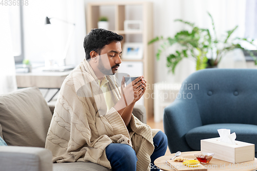 Image of sick young man in blanket drinking hot tea at home