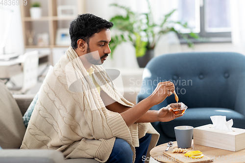 Image of sick young man in blanket drinking hot tea at home