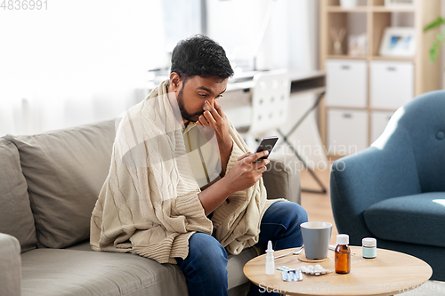 Image of sick young man in blanket with smartphone at home