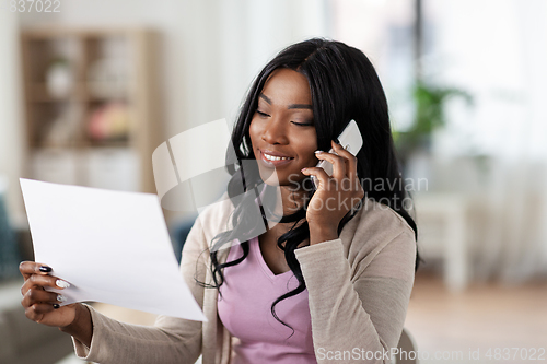 Image of woman with papers calling on phone at home office