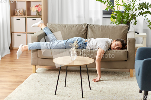 Image of bored or lazy young woman lying on sofa at home