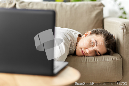 Image of bored woman with laptop lying on sofa at home