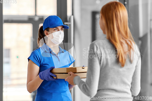 Image of delivery girl in mask giving pizza boxes to woman