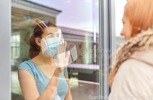 Image of ill woman in mask looking at friend through window
