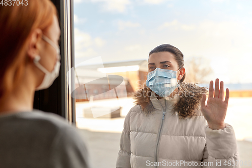 Image of woman in mask looking to friend through window