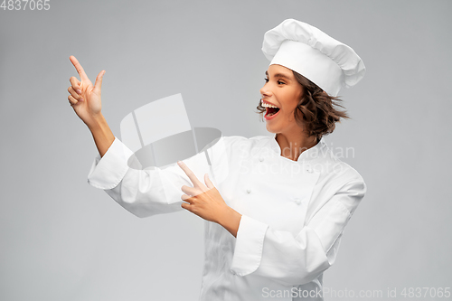 Image of smiling female chef in toque pointing finger up