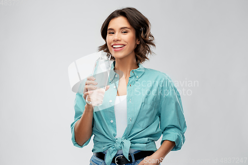 Image of smiling woman drinking water from glass bottle