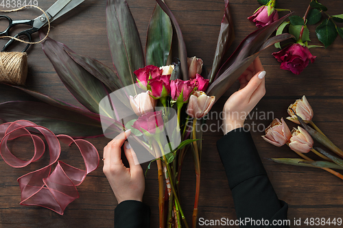 Image of Florist at work: woman making fashion modern bouquet of different flowers on wooden background