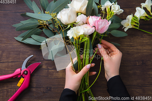 Image of Florist at work: woman making fashion modern bouquet of different flowers on wooden background