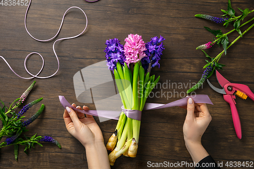 Image of Florist at work: woman making fashion modern bouquet of different flowers on wooden background