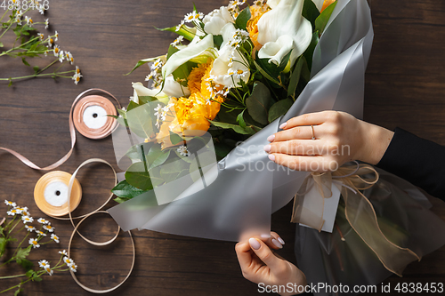 Image of Florist at work: woman making fashion modern bouquet of different flowers on wooden background