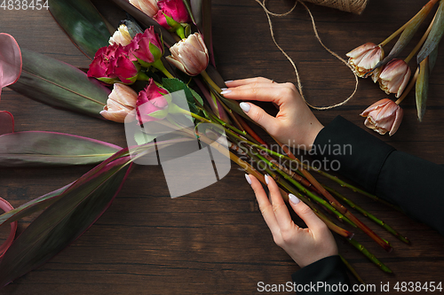 Image of Florist at work: woman making fashion modern bouquet of different flowers on wooden background