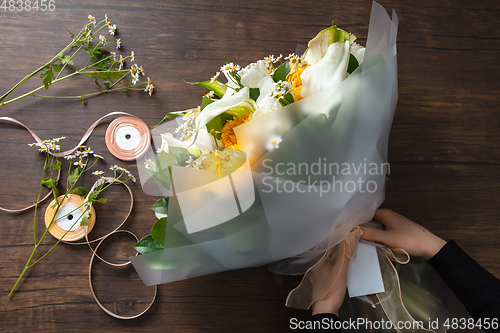 Image of Florist at work: woman making fashion modern bouquet of different flowers on wooden background