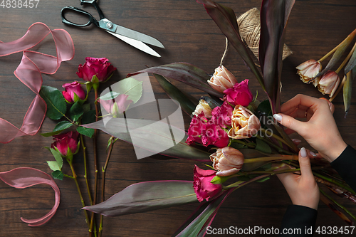 Image of Florist at work: woman making fashion modern bouquet of different flowers on wooden background