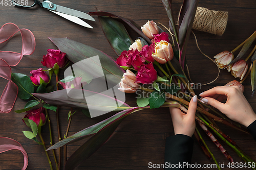 Image of Florist at work: woman making fashion modern bouquet of different flowers on wooden background