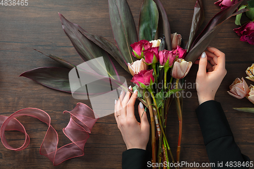 Image of Florist at work: woman making fashion modern bouquet of different flowers on wooden background