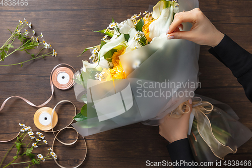 Image of Florist at work: woman making fashion modern bouquet of different flowers on wooden background