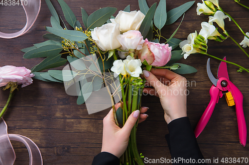 Image of Florist at work: woman making fashion modern bouquet of different flowers on wooden background