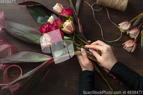 Image of Florist at work: woman making fashion modern bouquet of different flowers on wooden background