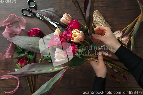 Image of Florist at work: woman making fashion modern bouquet of different flowers on wooden background