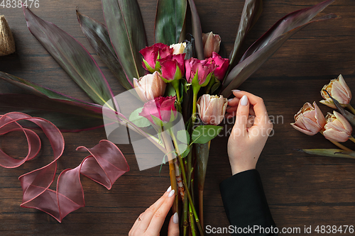 Image of Florist at work: woman making fashion modern bouquet of different flowers on wooden background