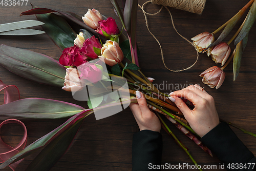 Image of Florist at work: woman making fashion modern bouquet of different flowers on wooden background