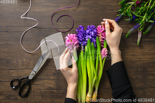 Image of Florist at work: woman making fashion modern bouquet of different flowers on wooden background