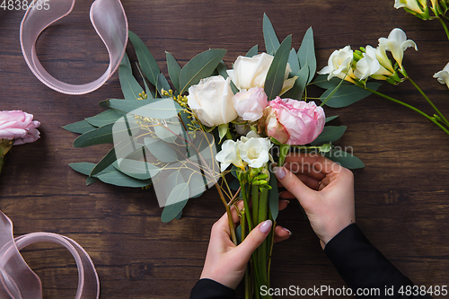 Image of Florist at work: woman making fashion modern bouquet of different flowers on wooden background