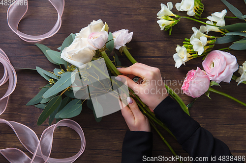 Image of Florist at work: woman making fashion modern bouquet of different flowers on wooden background