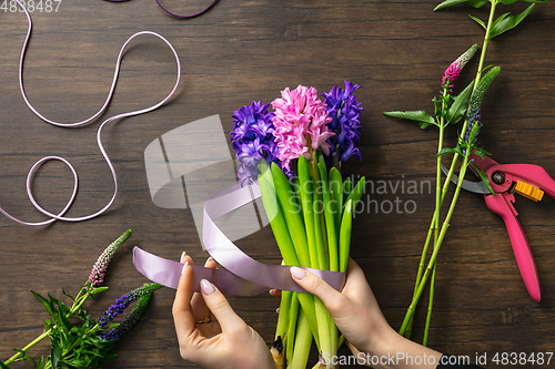 Image of Florist at work: woman making fashion modern bouquet of different flowers on wooden background