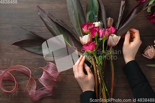 Image of Florist at work: woman making fashion modern bouquet of different flowers on wooden background