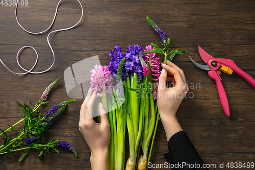 Image of Florist at work: woman making fashion modern bouquet of different flowers on wooden background
