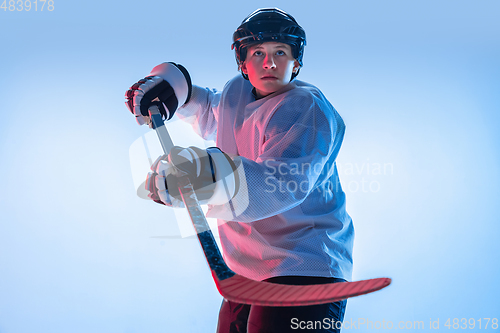 Image of Young male hockey player with the stick on ice court and white background in neon light
