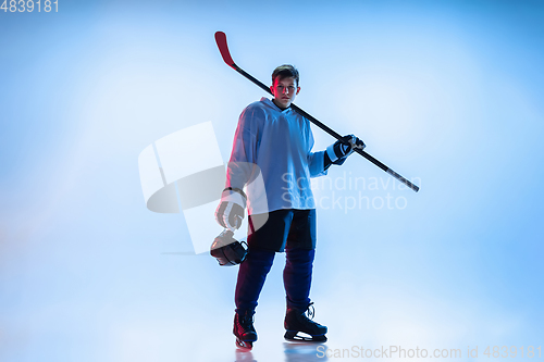 Image of Young male hockey player with the stick on ice court and white background in neon light