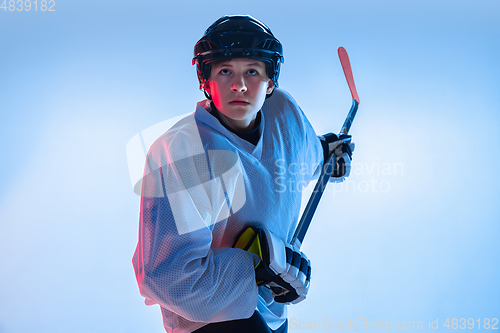 Image of Young male hockey player with the stick on ice court and white background in neon light