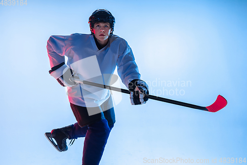 Image of Young male hockey player with the stick on ice court and white background in neon light