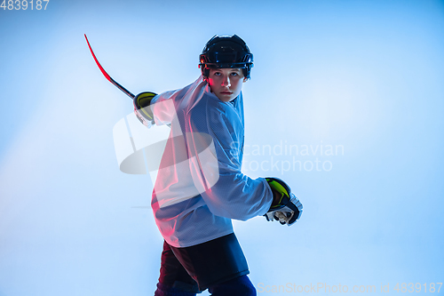 Image of Young male hockey player with the stick on ice court and white background in neon light