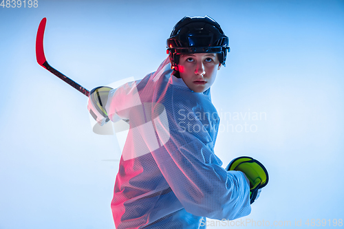 Image of Young male hockey player with the stick on ice court and white background in neon light