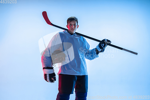 Image of Young male hockey player with the stick on ice court and white background in neon light