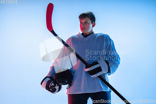 Image of Young male hockey player with the stick on ice court and white background in neon light